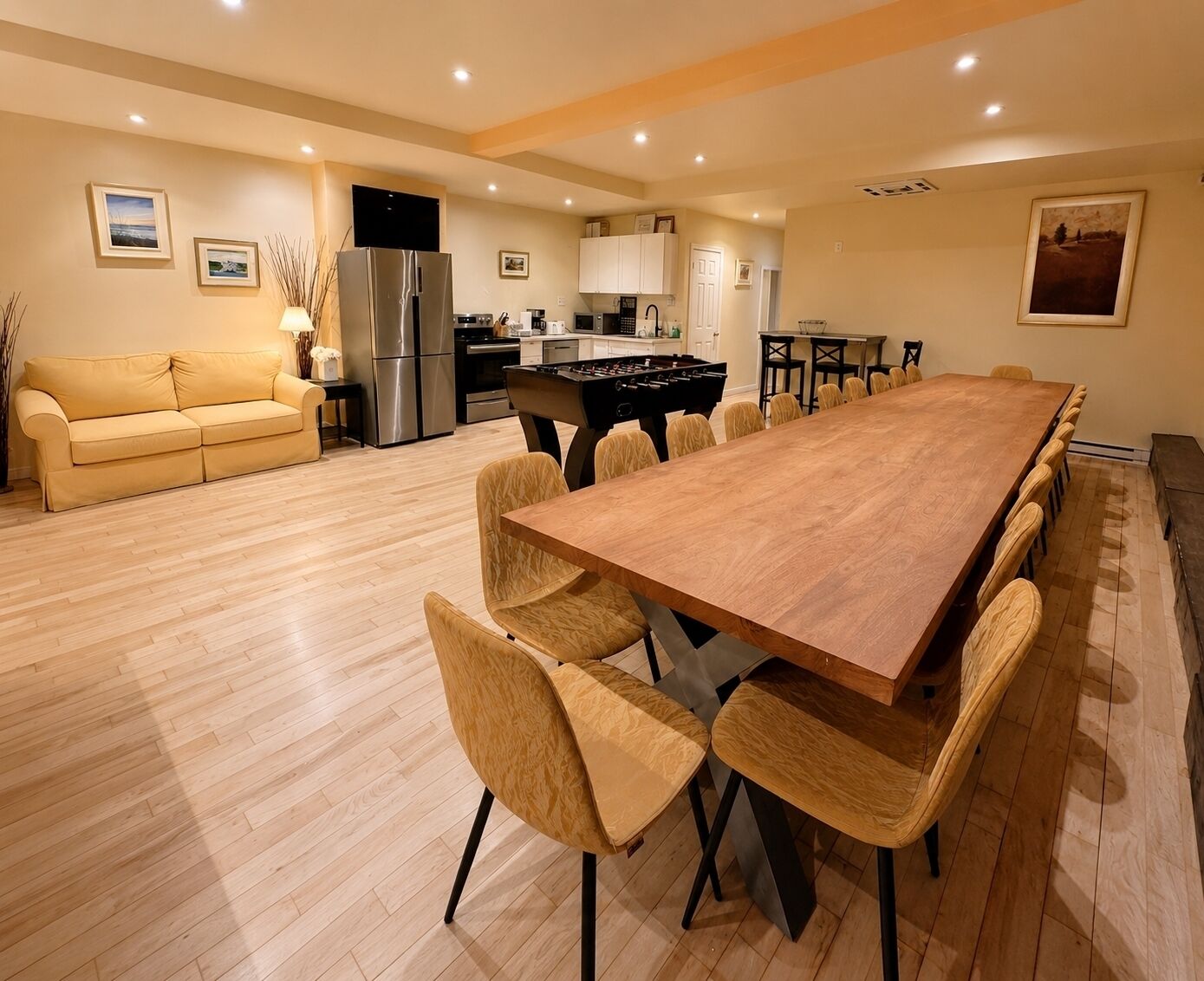 Amplia sala de estar con una larga mesa de comedor de madera rodeada de sillas, un sofá y una cocina con electrodomésticos modernos.