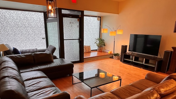 A modern living room with leather sofas, a glass coffee table, a flat-screen TV, and a large window with a view. - A1~Loft with Games~Gathering 20+ppl~100 Walk Score (Montréal)