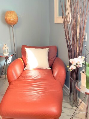 Un canapé en cuir rouge avec un coussin blanc, adossé à un mur bleu clair, une lampe sur pied et un vase contenant des orchidées blanches.