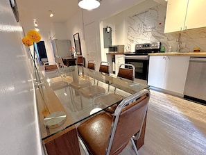A modern kitchen with a glass dining table, white cabinets, and a marble backsplash.