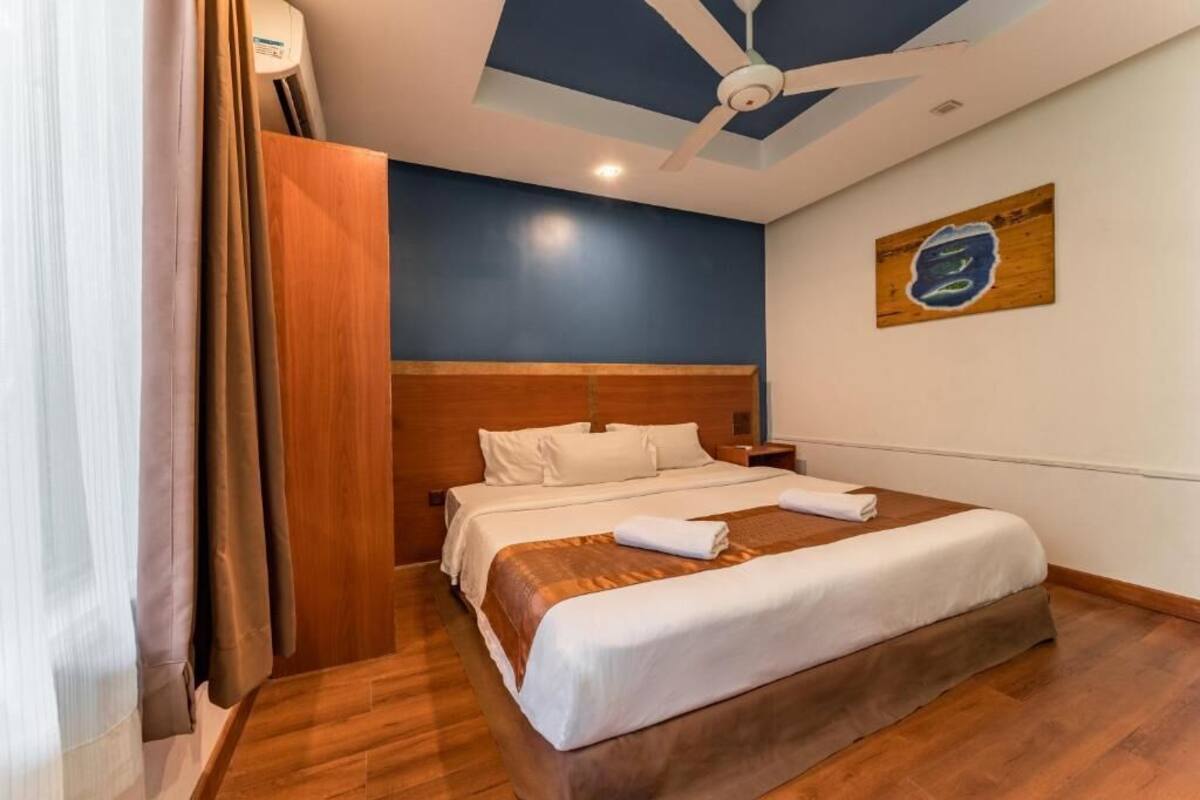 A hotel room with a wooden headboard, a ceiling fan, a bed with white linens, and a painting on the wall.