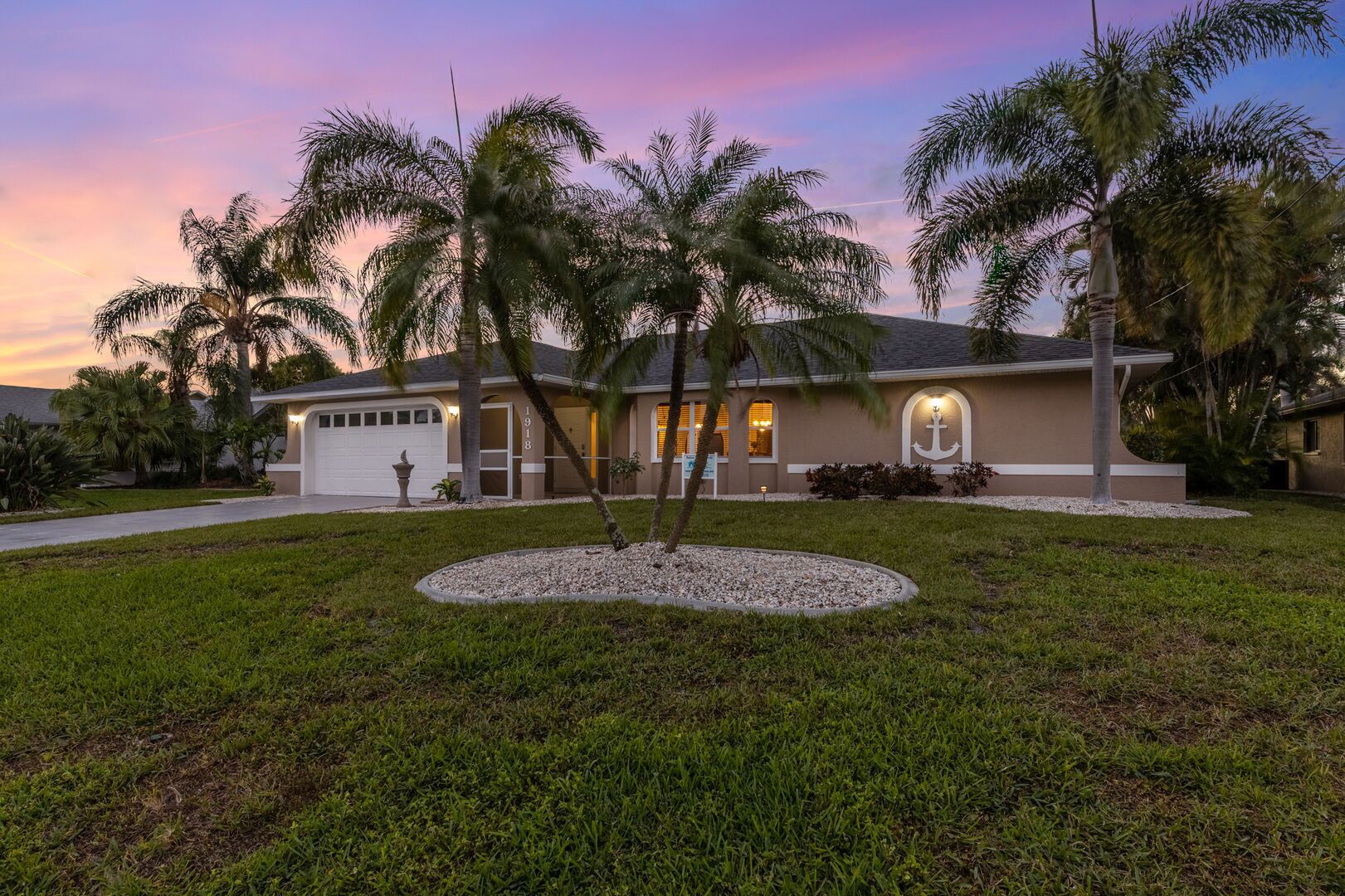 A residential house with a well-maintained lawn, palm trees, and a driveway.