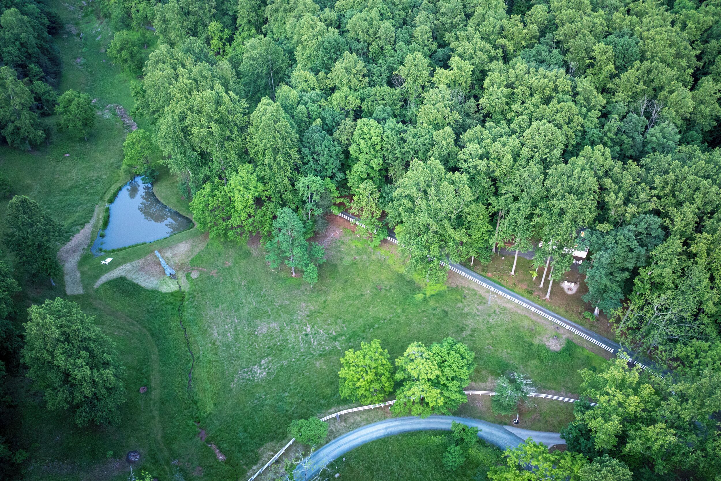 Une vue aérienne d’une zone boisée, avec une route sinueuse, un petit étang et un sentier bien tracé.