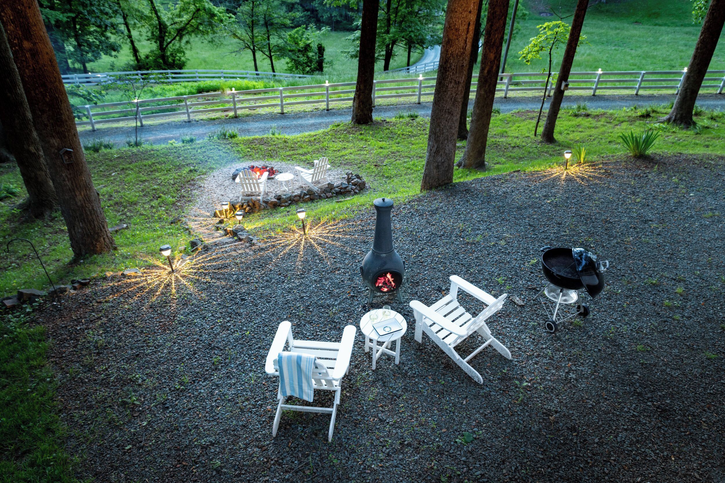 A gravel patio with outdoor seating, a fire pit, and a grill area.