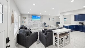 A modern living room with a fireplace, grey sofas, a dining table, and a kitchen area with blue cabinets. - Newly Renovated Luxury Home with an In-ground Pool in Tampa Bay! (Tampa)