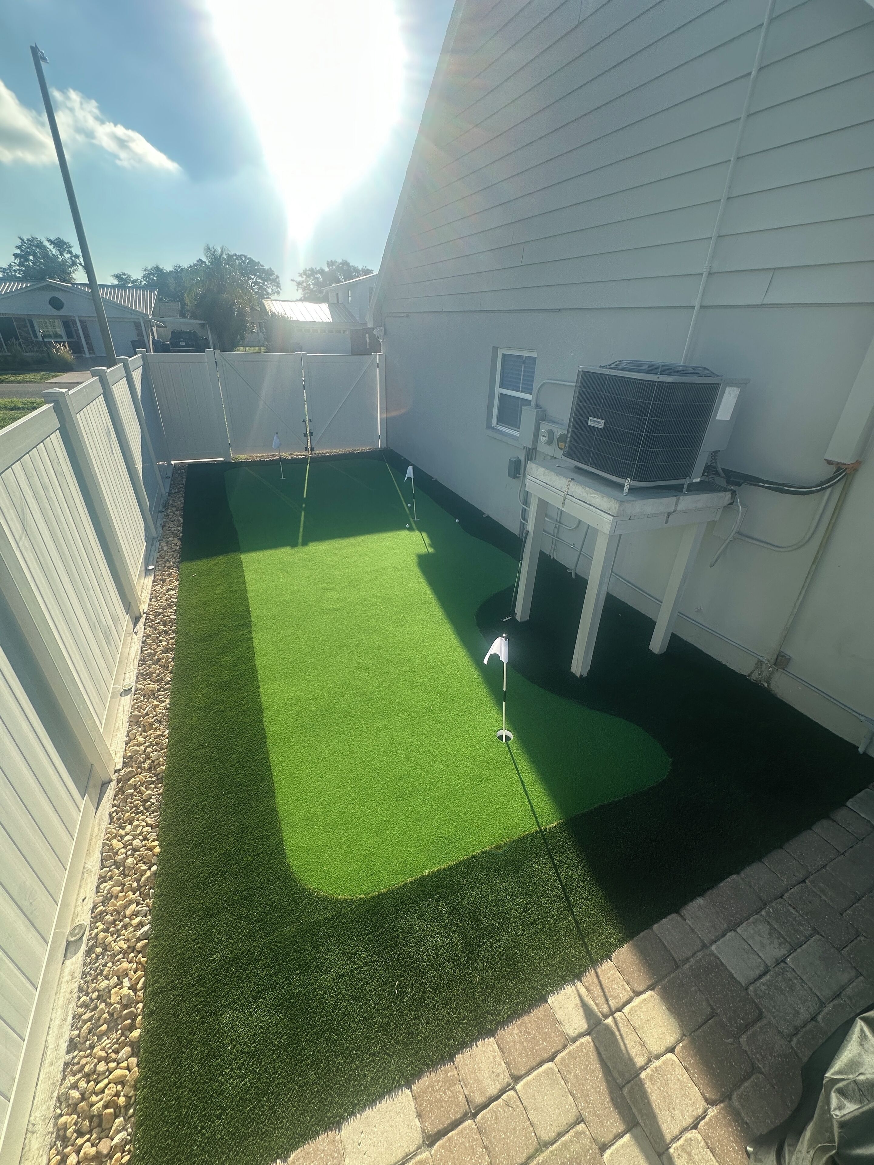 Un giardino sul retro con erba sintetica, una recinzione bianca e un piccolo deposito esterno bianco.