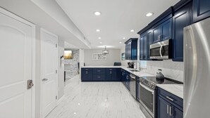 A modern kitchen with dark blue cabinets, stainless steel appliances, and a marble floor. - Newly Renovated Luxury Home with an In-ground Pool in Tampa Bay! (Tampa)