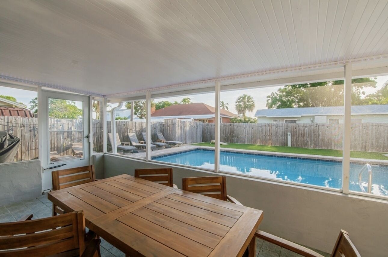Un patio cubierto con piscina, mesa y sillas de madera.