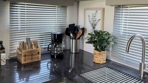 A kitchen with light wood cabinets, a black countertop, a coffee maker, a utensil holder, and a potted plant. - Fully Equipped Camper-Quiet Campground near Medora (Belfield)