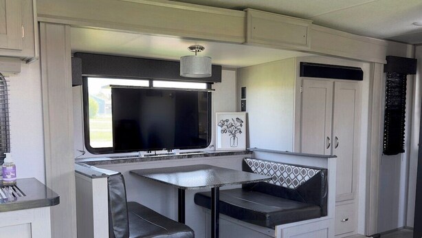 A compact RV kitchen with a dining area, a TV, and a small seating space. - Fully Equipped Camper-Quiet Campground near Medora (Belfield)