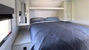 A compact, well-lit room with a bed, storage cabinets, and a window. - Fully Equipped Camper-Quiet Campground near Medora (Belfield)
