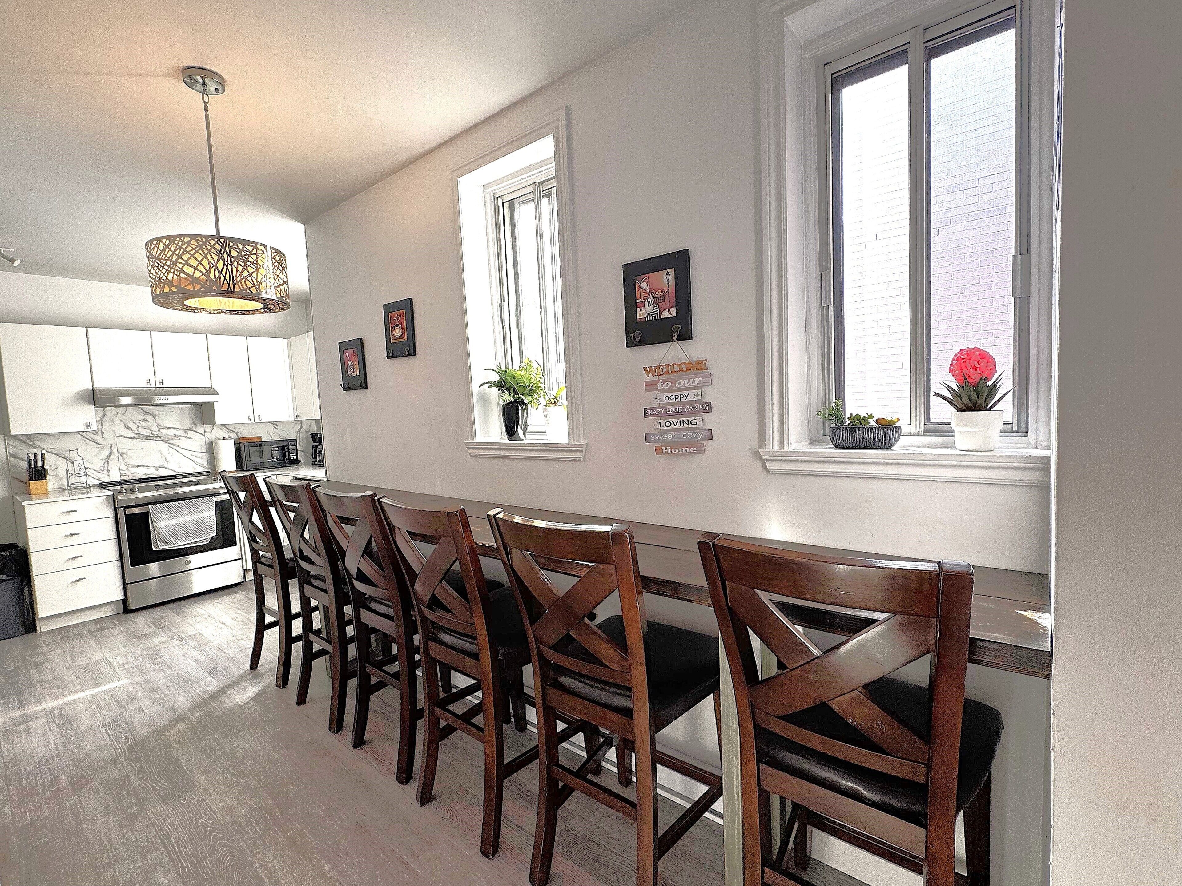 A kitchen with a dining area, wooden chairs, a stove, and a window with plants.