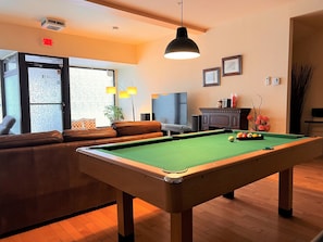 A pool table in a room with a sofa, a television, and a fireplace.