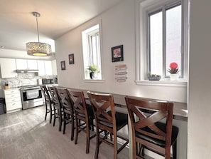 A kitchen with a dining area, wooden chairs, a stove, and a window with plants. - B23~Sunny Terrace+17 Bed/Sofa bed+6 Room+6 Full Bath+Free parking~100 WalkScore (Montréal)