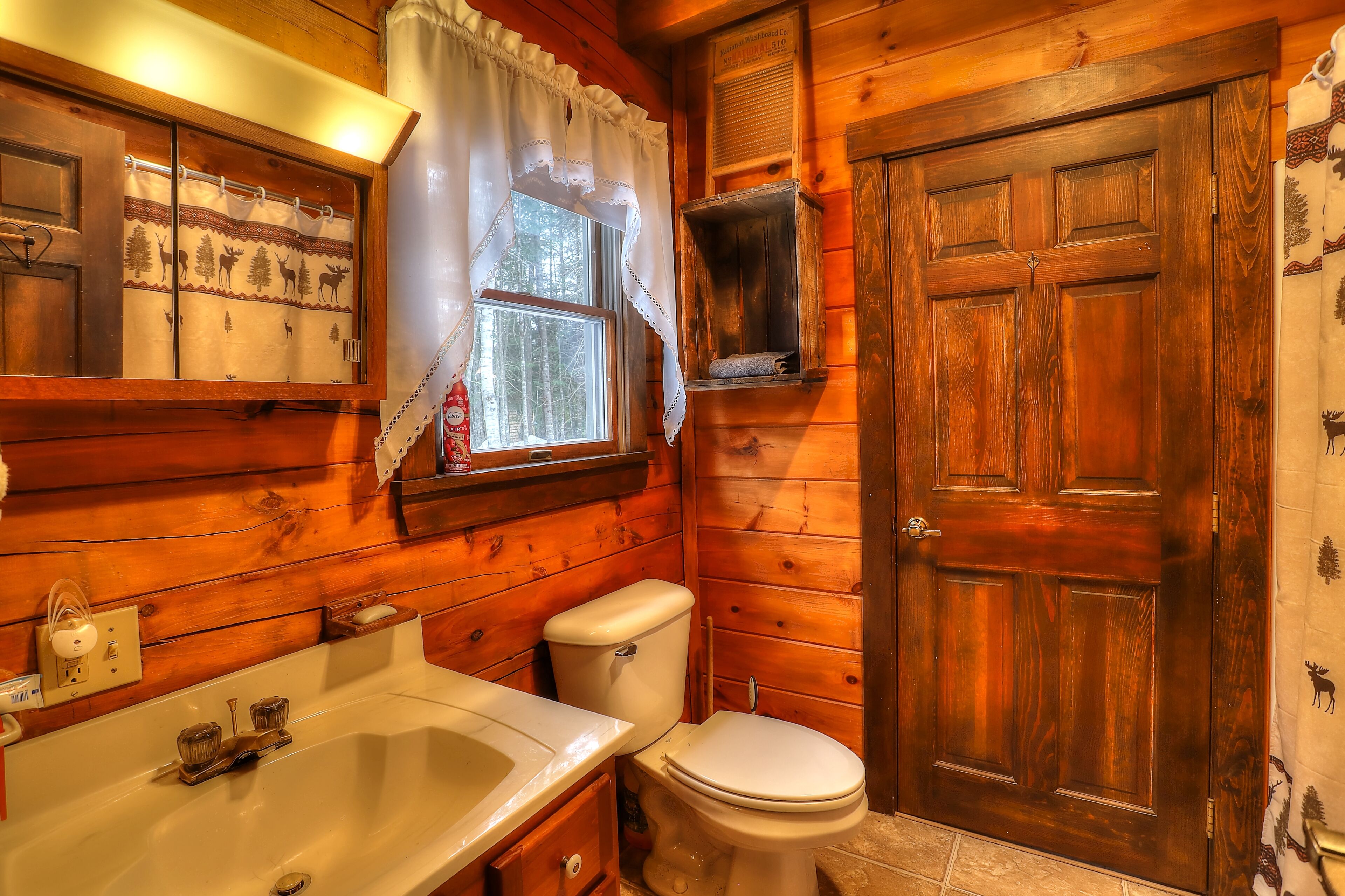 A wooden cabin bathroom with a toilet, sink, and window.