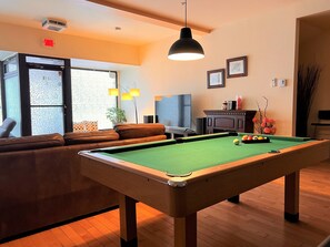 Una mesa de billar en una sala con un sofá, una televisión y una chimenea.
