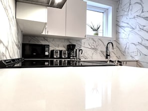 Una cocina moderna con microondas, tostadora y cafetera sobre la encimera, un lavabo y una ventana con una planta en el alféizar.