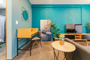 Un salon moderne avec un mur d’accent de couleur turquoise, un bureau en bois, un téléviseur et un canapé.