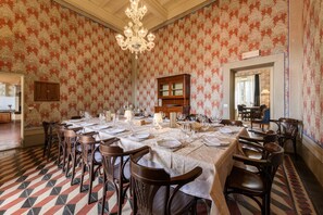 A dining room with a large table set for six, surrounded by wooden chairs, a chandelier, and patterned wallpaper.