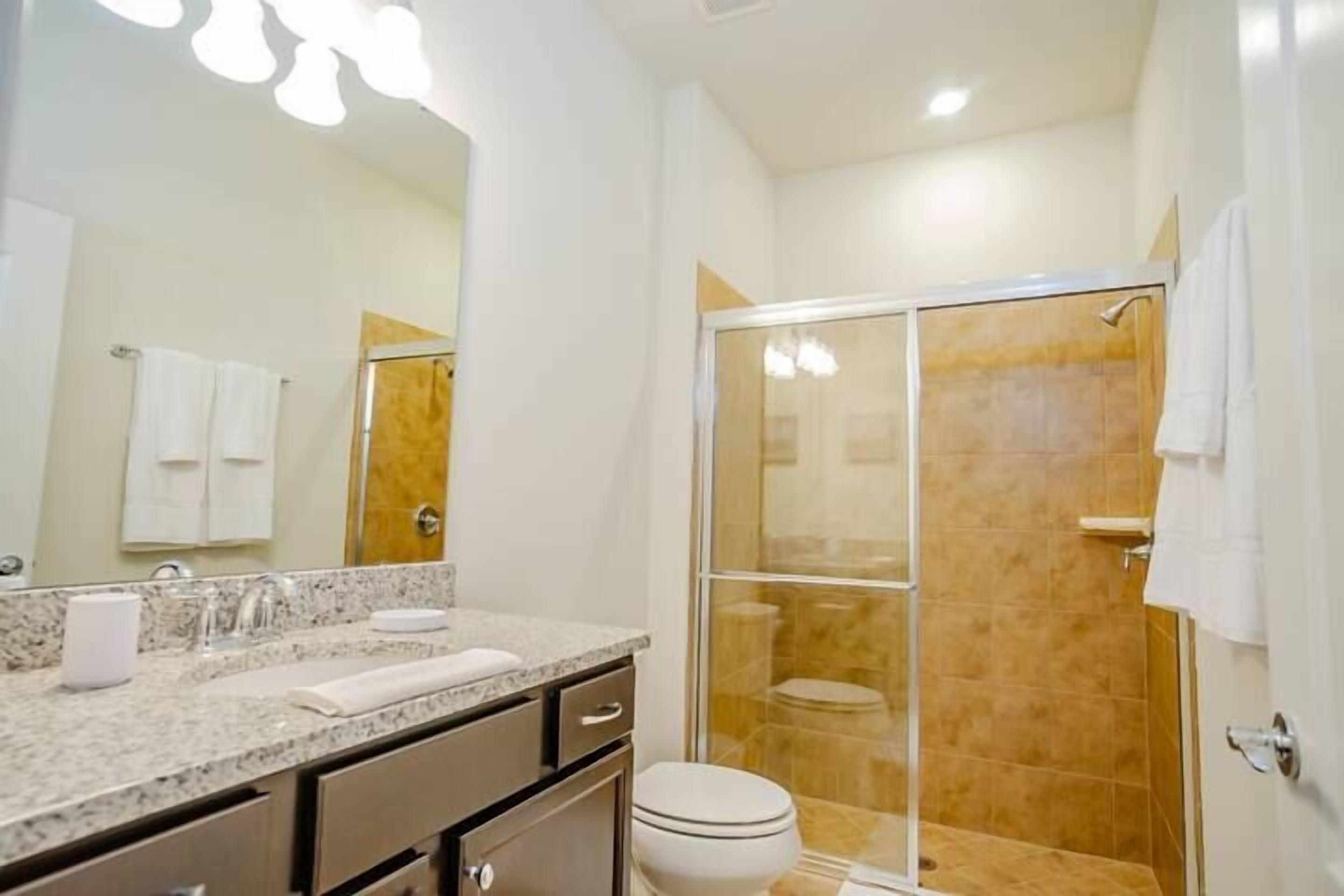 A bathroom with a marble countertop, a toilet, and a glass-enclosed shower.