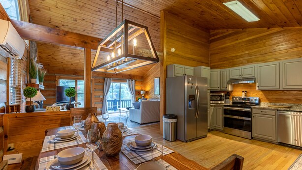 A cozy cabin with a wooden interior, a dining area set for four, and a kitchen with modern appliances. - Horse Valley Lodge - Pool Table, Firepit, Indoor fireplace, Pet Friendly (Boone)