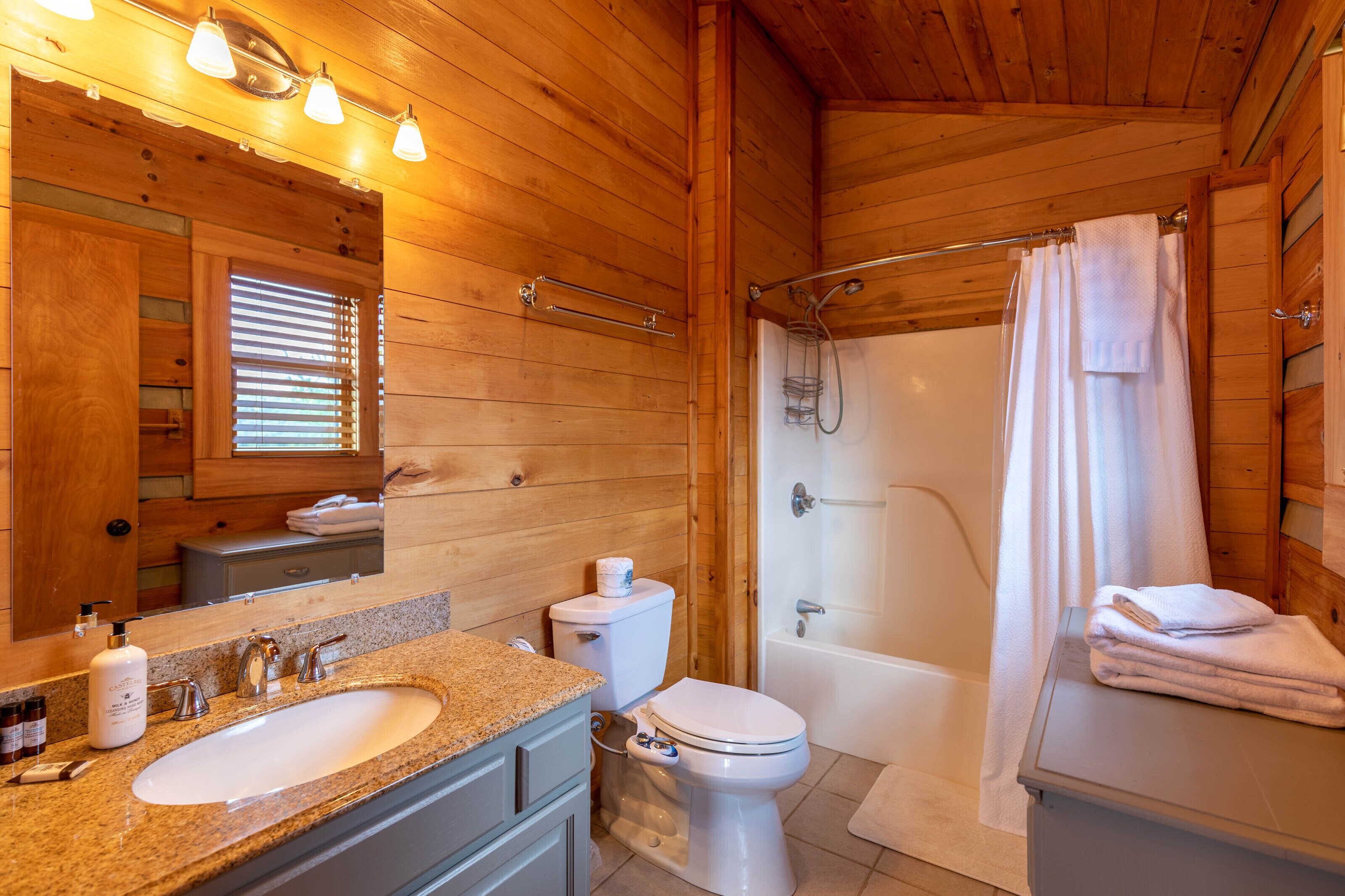 Une salle de bain rustique, aménagée dans une cabane en bois, avec un lavabo, des toilettes et une douche.