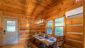 A wooden cabin interior with a dining table set for four, benches, and a hanging light fixture. - Horse Valley Lodge - Pool Table, Firepit, Indoor fireplace, Pet Friendly (Boone)