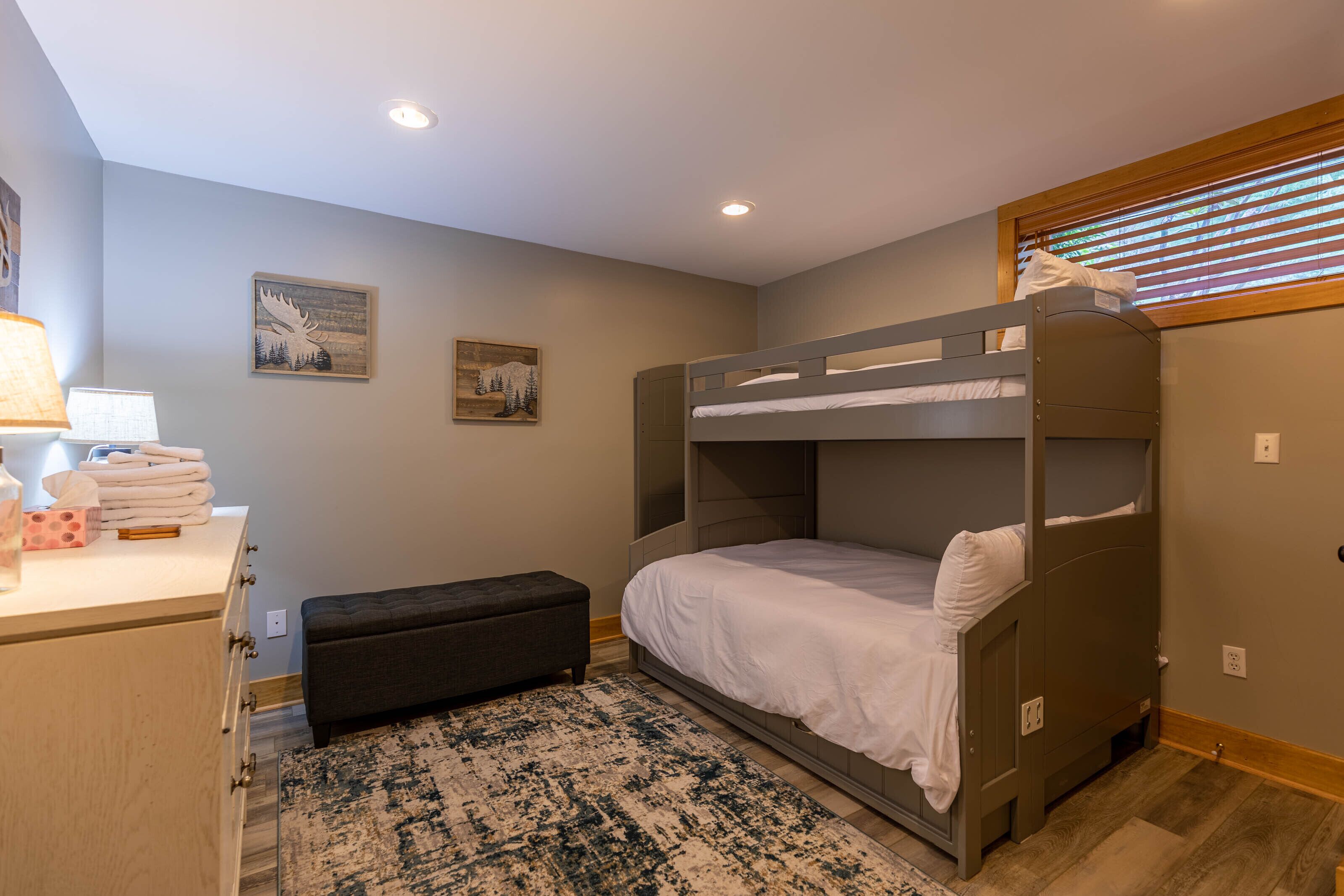 A bunk bed room with a desk, lamp, and artwork on the walls.
