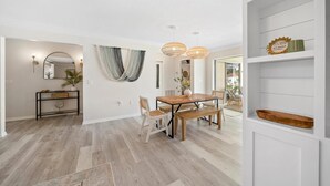 A modern dining area with a wooden table and chairs, a console table with a mirror and decorative items, and a white shelving unit with storage baskets.