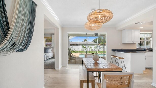 A modern kitchen with white cabinets, a wooden dining table, and a wicker pendant light.