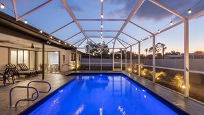 An indoor swimming pool with a glass ceiling, lounge area with chairs, and a view of the surrounding landscape.