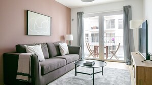 Un salon moderne avec un canapé gris, une petite table basse ronde et un téléviseur posé sur un meuble en bois.