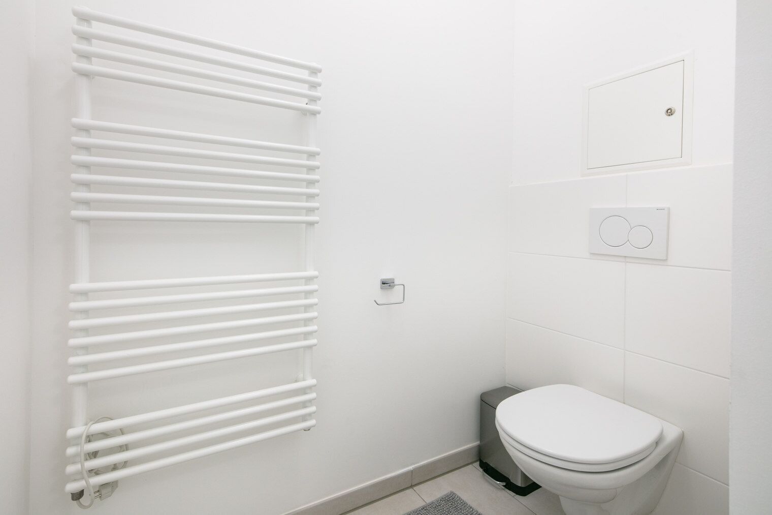 Et moderne badeværelse med en hvid radiator, et toilet og et panel til styring på væggen.