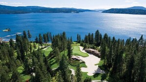 A golf course with a large body of water in the background, surrounded by dense forest. - Lake CDA: Soak, Paddle, Dock & Unwind (Coeur D Alene)