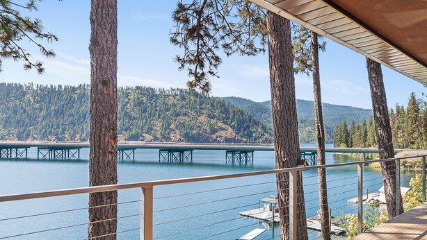 A deck with a wooden table and bench overlooking a lake, with a bridge in the background. - Lake CDA: Soak, Paddle, Dock & Unwind (Coeur D Alene)