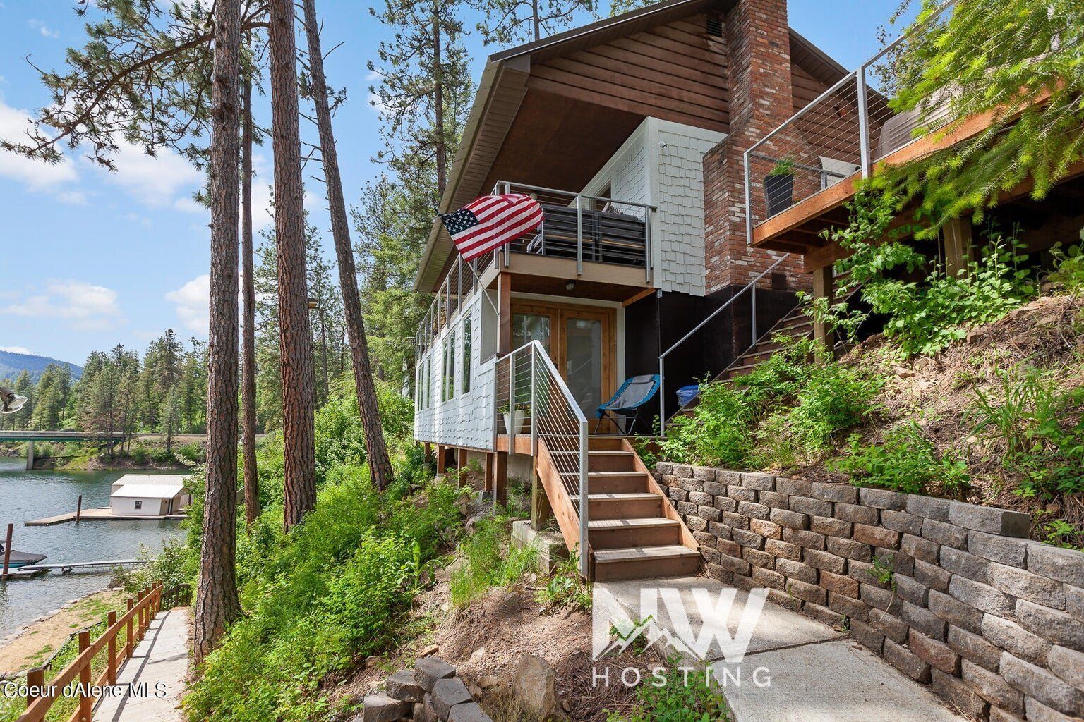 A modern two-story house with a balcony, a wooden deck, and a view of a lake.