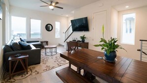 A modern living room with a sofa, a dining table, a TV, and a staircase. - San Diego Beachfront House 60s to sand, surf, pier (Imperial Beach)