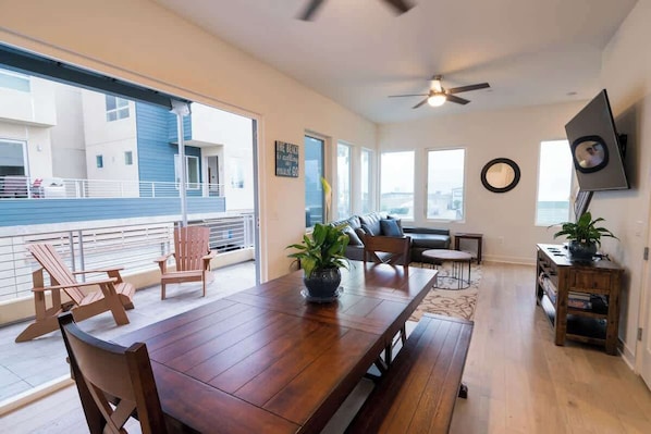 A spacious living area with a wooden dining table, chairs, a sofa, and a ceiling fan.