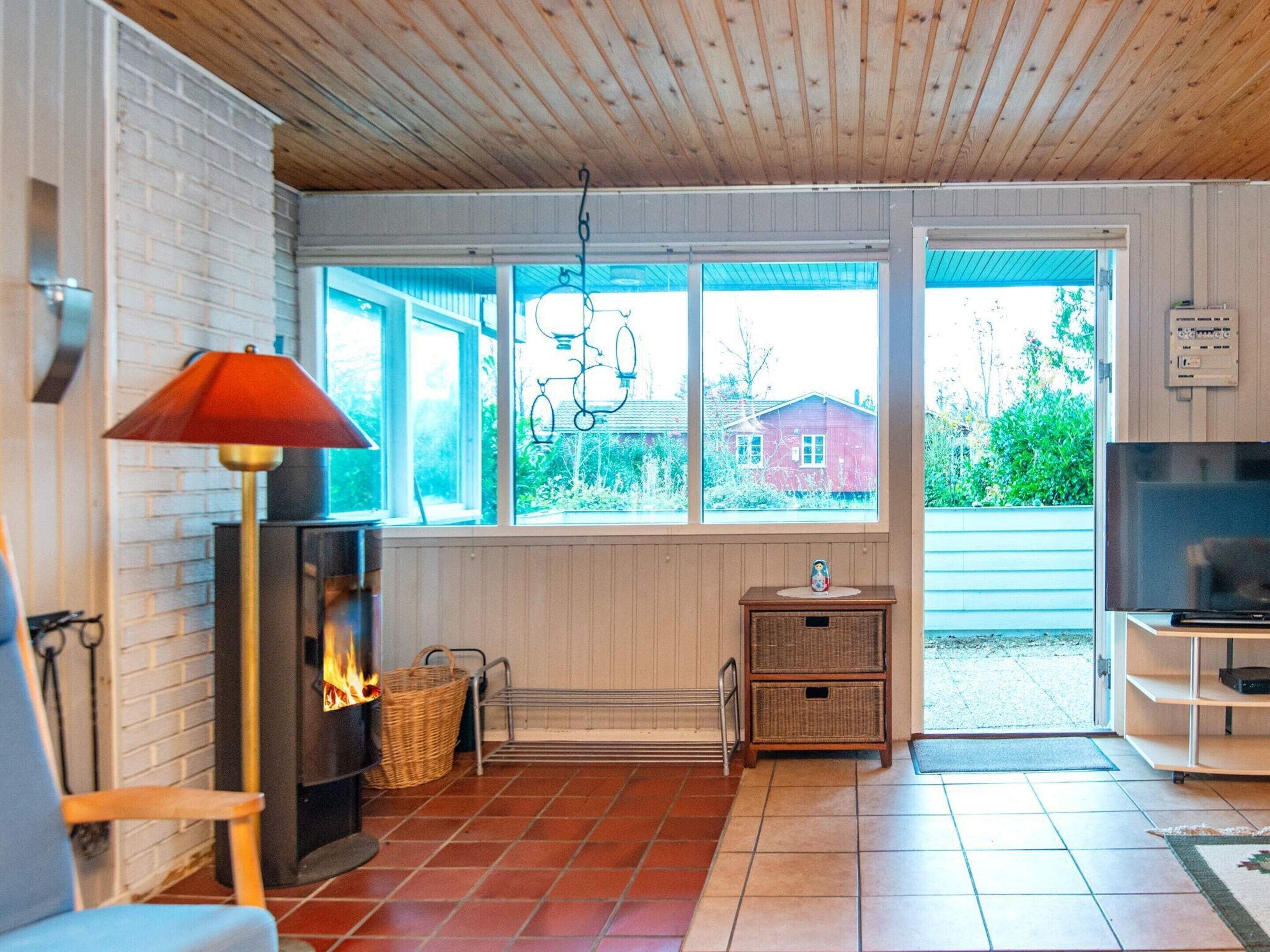 Ein gemütliches Wohnzimmer mit Kamin, Fernseher und einem großen Fenster mit Blick auf ein Haus und Grünflächen.