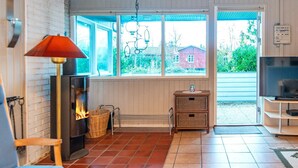 A cozy living room with a fireplace, a television, and a large window with a view of a house and greenery. - 5 Person Holiday Home in Sydals (Sydals)