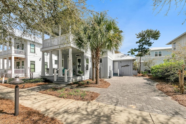 A residential street with white houses, a covered porch, and a paved walkway.