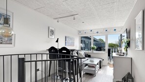 En modern inredning med matplats, kök och vardagsrum, med bland annat en trappa, räcken och stora fönster.
