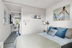A bedroom with a bed, a desk, and a chair. There is a painting on the wall and a shelf with books.