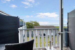A balcony with a view of a grassy yard and a distant building. - Holiday in the first row to the water (Dannemare)