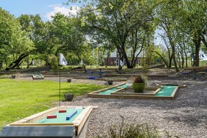 A miniature golf course with multiple holes, surrounded by trees and a building in the background.