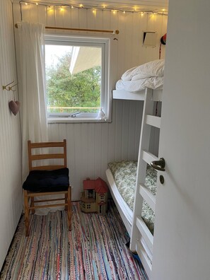 Ein Zimmer mit Etagenbett, einem Holzbett, einem Spielzeughaus und einem Fenster mit Vorhängen.