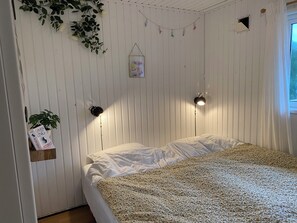 Makuuhuoneessa on sänky, kaksi seinälle asennettua lamppua, kirjahylly, amppelissa roikkuva kasvi ja pieni ikkuna.
