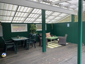 Ein überdachter Patio-Bereich mit Tisch und Stühlen, einer hängenden Pflanze und einem Schild mit der Aufschrift 'Love the Beach'.