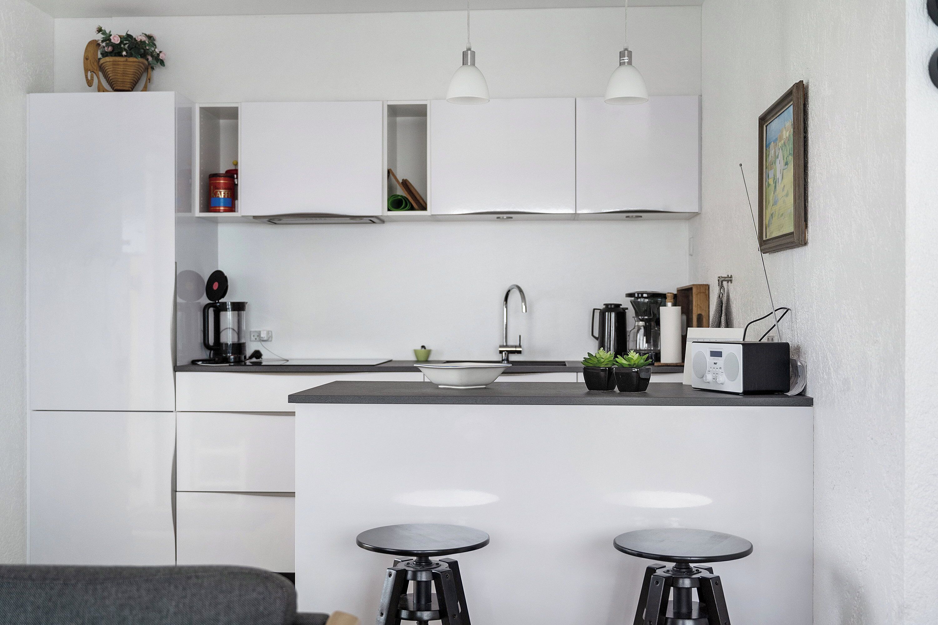 A modern kitchen with white cabinets, a central island with stools, a coffee machine, and a radio.