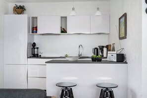 Una cocina moderna con armarios blancos, una isla central con taburetes, una cafetera y un radio.